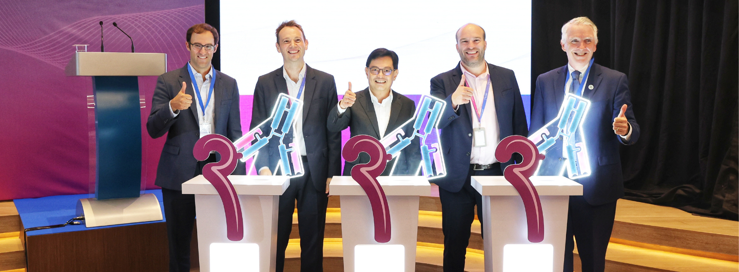 Five people give thumbs-up by tables with graphic of 2 and antibody illustration.